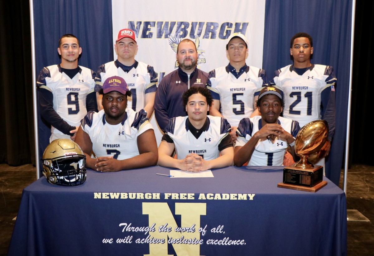 Eight students who signed to play football in college with their coach.