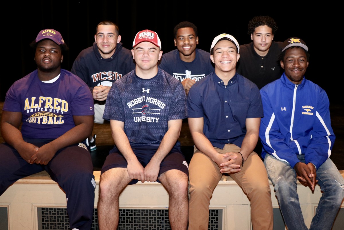 Eight students who signed to play football in college in their college gear.
